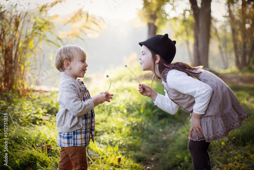 Dzieci dmuchają dmuchawce w parku przy letnim słoneczku © Katarzyna Krociel
