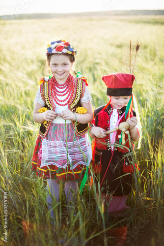 Dzieci w tradycyjnych polskich krakowskich strojach spacerują po polu obsianym zbożem w ciepłych letnich promieniach słonca