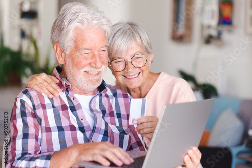 Elderly couple browsing by laptop enjoying shopping online. Joyful and smiling beautiful senior couple indoors being in great mood using credit card to purchase © luciano