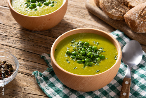 Green pea soup in a wooden bowl on rustic wooden table	