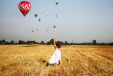 Dziewczynka biegnie po polu i macha do balonów na gorące powietrze, lot balonem nad polami w środku lata