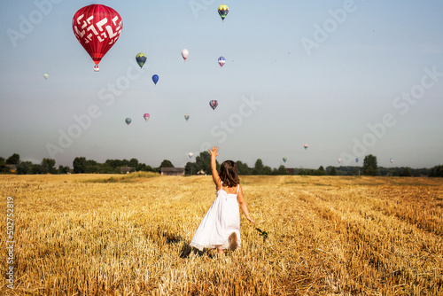 Dziewczynka biegnie po polu i macha do balonów na gorące powietrze, lot balonem nad polami w środku lata