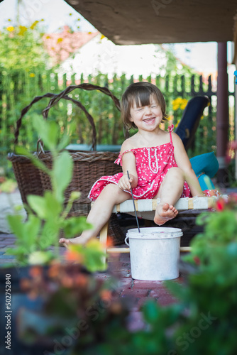 Wesoła dziewczynka moczy nogi w wiadrze z wodą, zabawa w gotowanie zupy zkwiatów