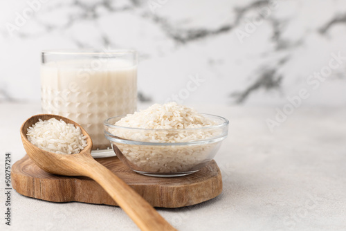 Glass cup of rice milk with a bowl of rice on a light background