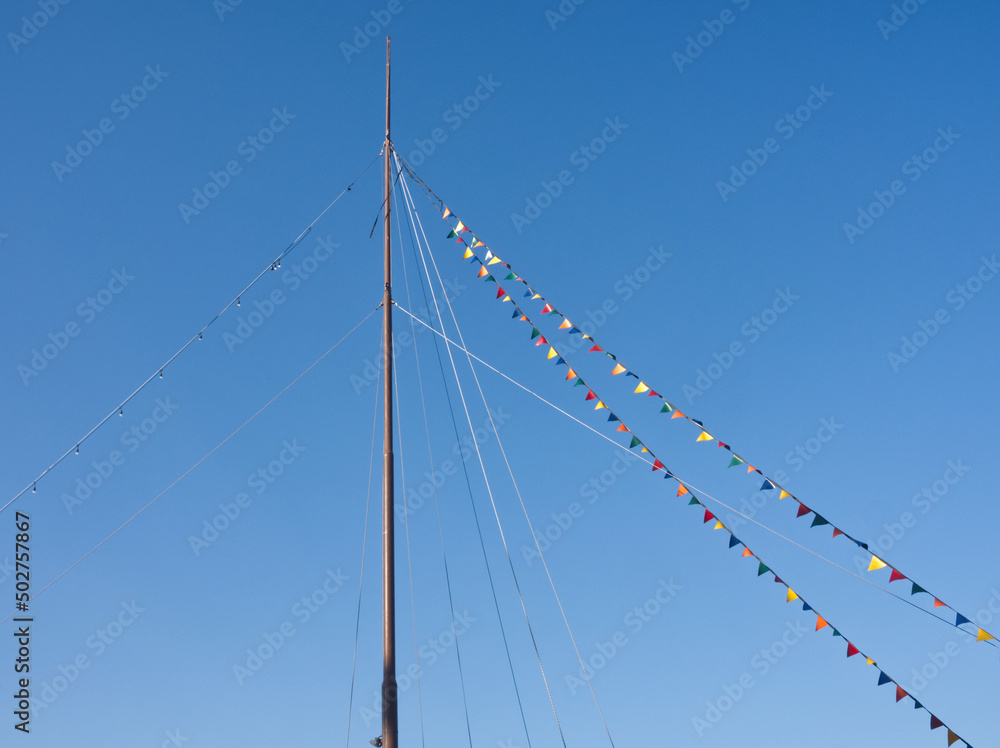 Boat mast draped in colorful flags and pennants on blue sky background. Triangle flag and bunting on ship or yacht lines. Travel and vacation layout, copy space for text. Sea, nautical greetings card. Boat mast draped in colorful flags and pennants on blue sky background. Triangle flag and bunting on ship or yacht lines. Travel and vacation layout, copy space for text. Sea, nautical greetings card.