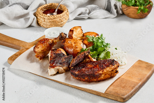Roasted chicken with spices and herbs on wooden plate. Traditional caucasian food - chicken tabaka. Grilled chicken with bread and sauce on concrete background.