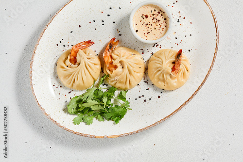 Steamed dumplings shrimp in asian style on white concrete background. Prawn dim sum with sauce on ceramic plate. Shrimp wontons on dish in minimal style. Asian dumplings with seafood.