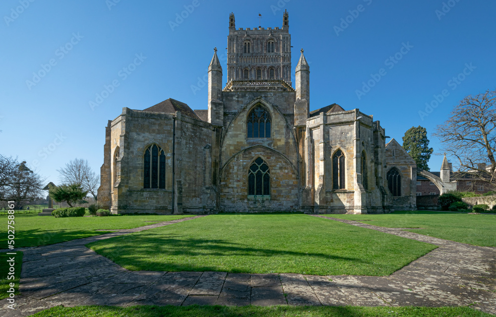 A low wide angle image of Tewkesbury Abbey with the beautiful green grass and paved foreground and clear blue skies.