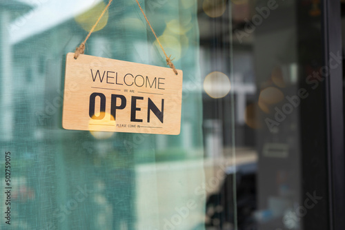 Open and closed flip sign in front of coffee shop and restaurant glass door. Wooden sign with wording of place's status. Say Welcome.