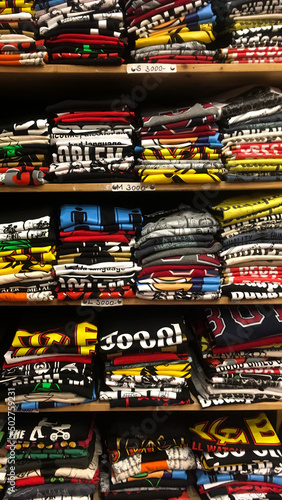A large assortment of bright cotton T-shirts neatly folded on the shelf. Fresh T-shirts of different sizes stacked on a display case with shelves.