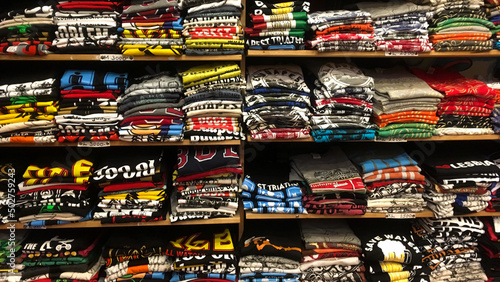 A large assortment of bright cotton T-shirts neatly folded on the shelf. Fresh T-shirts of different sizes stacked on a display case with shelves.