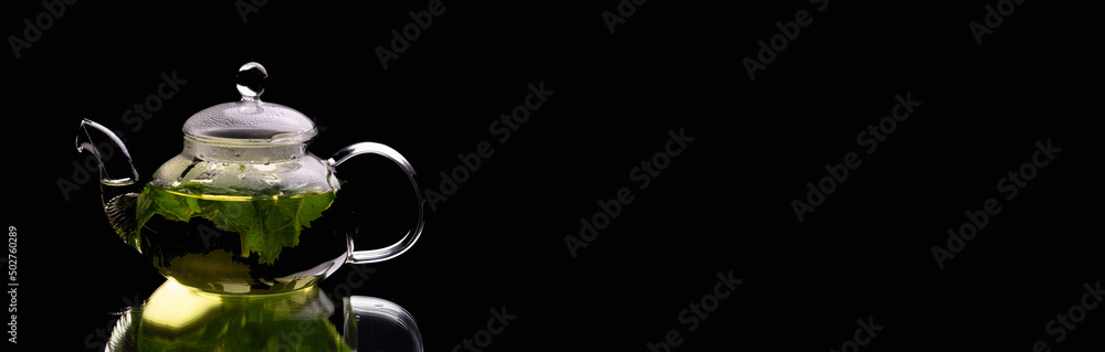 Hot glass teapot on a black background banner and place for advertising - green mint tea. Herbal tea and healthy drink concept. Hot glass teapot on a black background banner and place for advertising - green mint tea. Herbal tea and healthy drink concept.