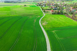 Droga polna przebiegająca przez pola i łąki widziana z wysokości. Zdjęcie z drona. W oddali widać zabudowania pobliskiej wioski.