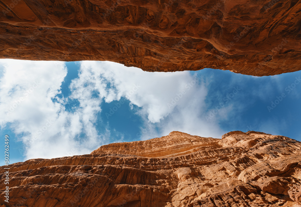 Looking up red sandstone canyon in Wadi Rum desert, blue sky with clouds above - obrazy, fototapety, plakaty 