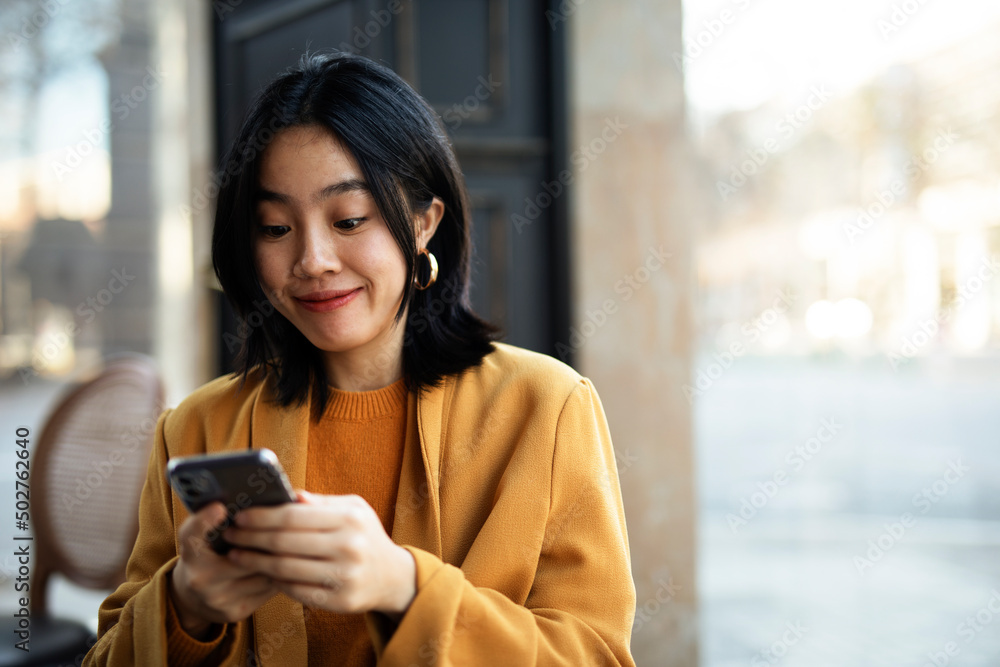 Fototapeta premium Happy Chinese girl checking phone. Beautiful young girl typing a message