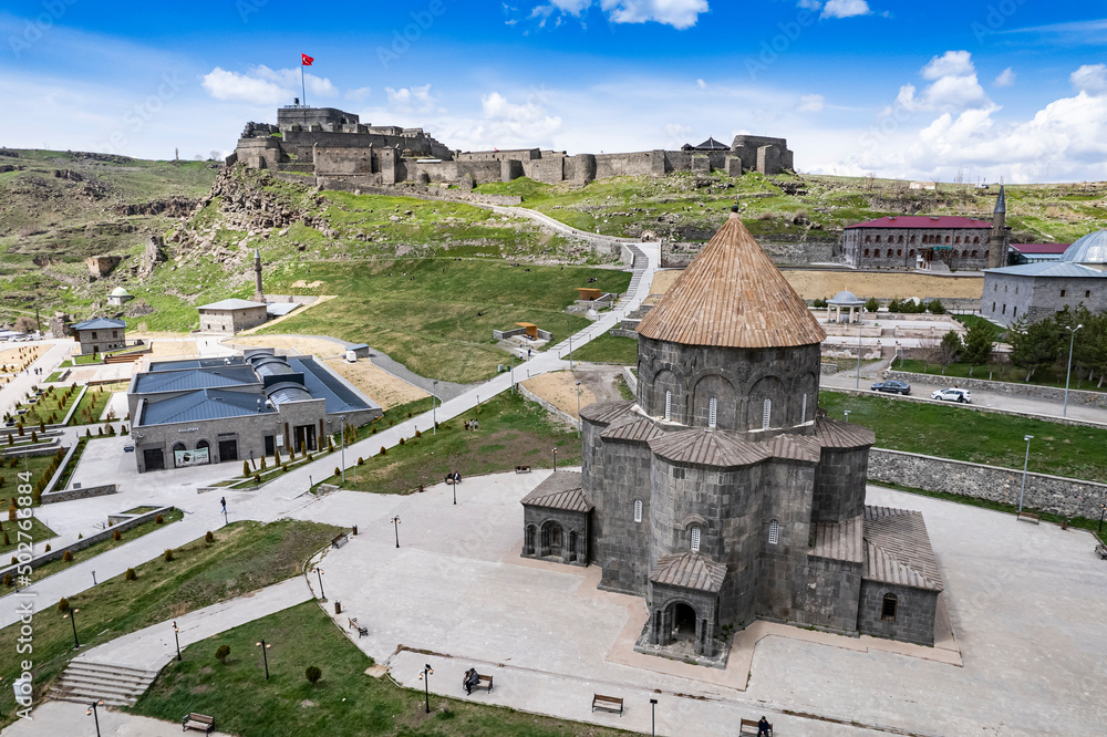 Fototapeta premium Ancient stone bridge across Kars River & Kars Castle - main tourist attractions of Kars, Turkey. Near flag (on castle) are portrait of Ataturk & writing in Turkish 'Motherland remembers you'
