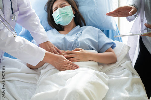 Group of Doctor try to help patient woman lie on hospital bed and holding on stomach suffering. Abdominal pain that comes from menstruation, diarrhea, or indigestion. Sickness and healthcare concept