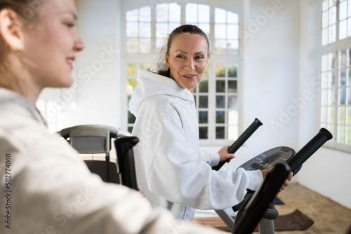 Woman talking to her teen daughter while using modern elliptical machine