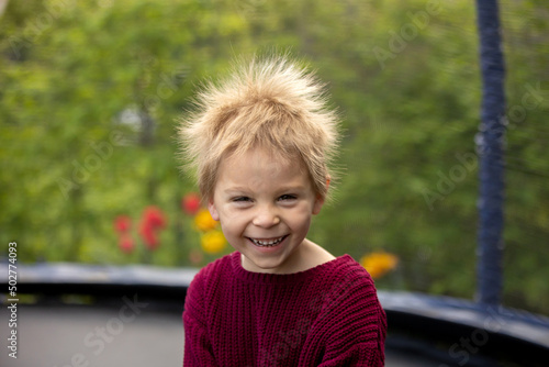 Cute little boy with static electricy hair, having his funny portrait taken outdoors on  trampoline