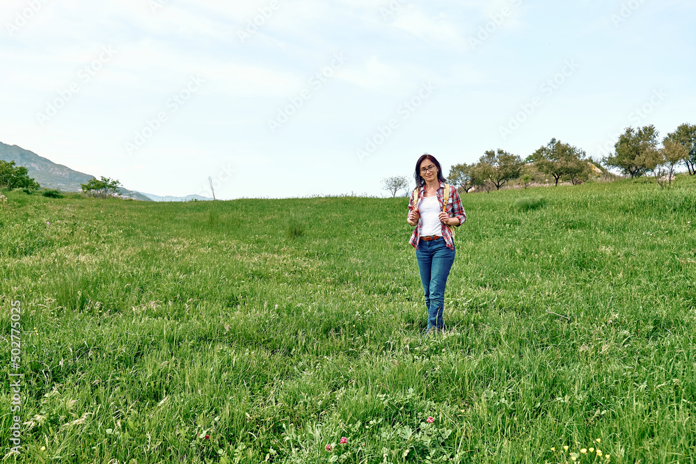 Happy beautiful carefree woman walking on a spring meadow with green grass. Hiking outdoors, unity with nature. Happy beautiful carefree woman walking on a spring meadow with green grass. Hiking outdoors, unity with nature.