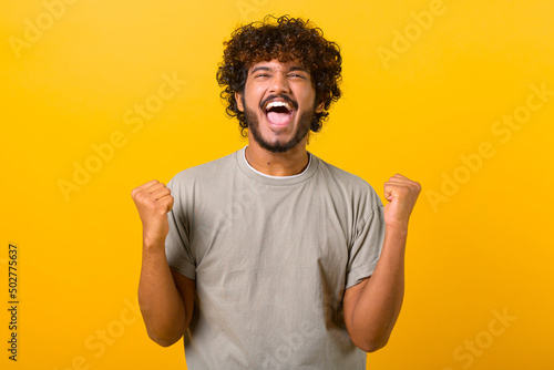 Stampa su tela Overjoyed crazy happy Indian curly guy screaming yes in ecstatic, raising fists up, celebrating good luck, victory, isolated on yellow