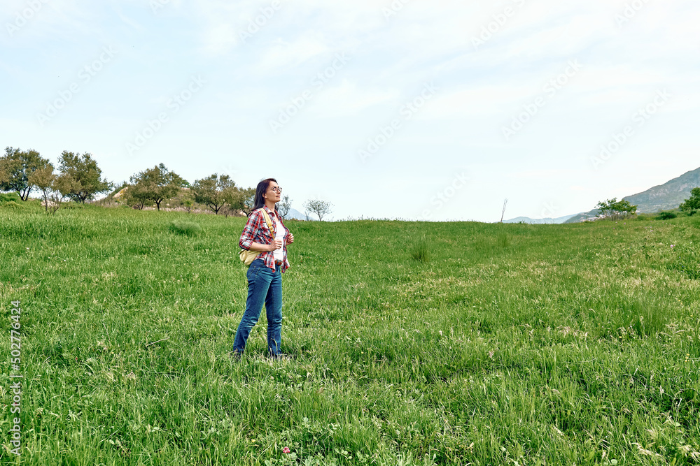 Happy beautiful carefree woman walking on a spring meadow with green grass. Hiking outdoors, unity with nature. Happy beautiful carefree woman walking on a spring meadow with green grass. Hiking outdoors, unity with nature.