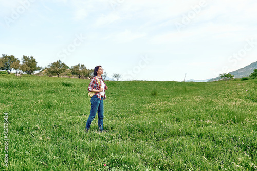Happy beautiful carefree woman walking on a spring meadow with green grass. Hiking outdoors, unity with nature.