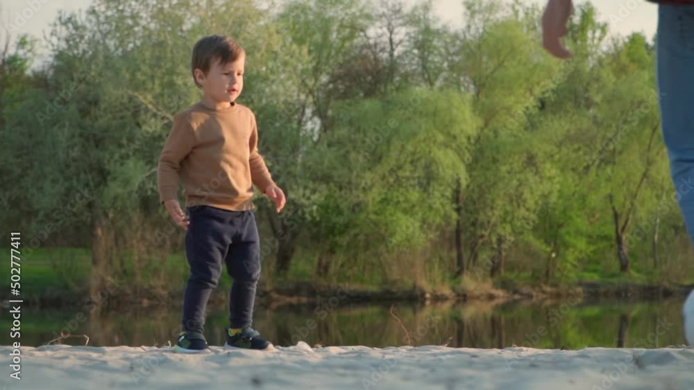 Little Kid Kicks Soccer Ball to His Father. Slow Motion. Young Man And Little Boy Playing With Black and White Football Ball Outdoors Little Kid Kicks Soccer Ball to His Father. Slow Motion. Young Man And Little Boy Playing With Black and White Football Ball Outdoors