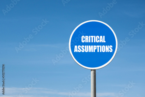 'Critical assumptions' sign in blue round frame. Blue sky is on background