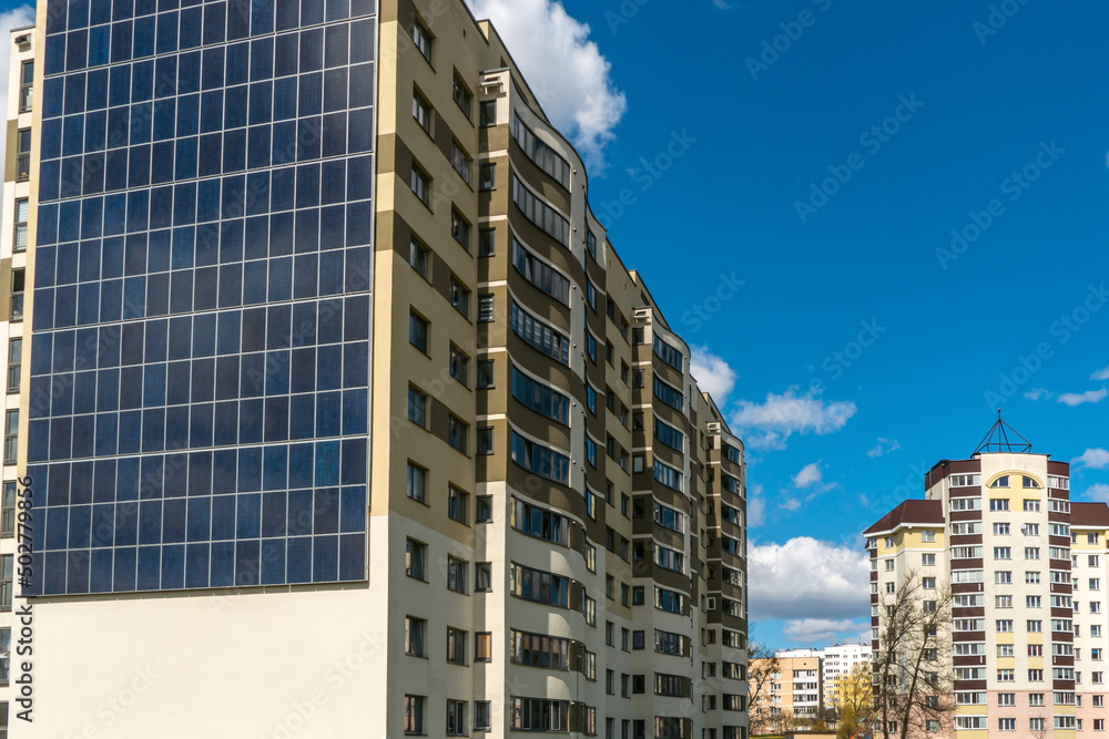 Obraz premium Movement of clouds against the background of a modern energy-efficient building. Multi-storey residential building with solar panels on the wall. Renewable energy in the city