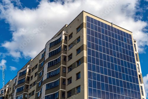 Movement of clouds against the background of a modern energy-efficient building. Multi-storey residential building with solar panels on the wall. Renewable energy in the city