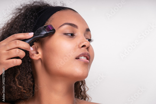 Confident young Hispanic lady doing face massage with derma roller photo