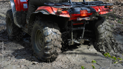 Close-up of the red ATV riding through the muddy woods. Rear view. Extreme type of outdoor activities. Riding on a quad bike.