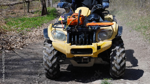 Close-up of a yellow quad bike riding on a forest dirt road. Front view. Extreme type of outdoor activities. Tourist trips on an quad bike.