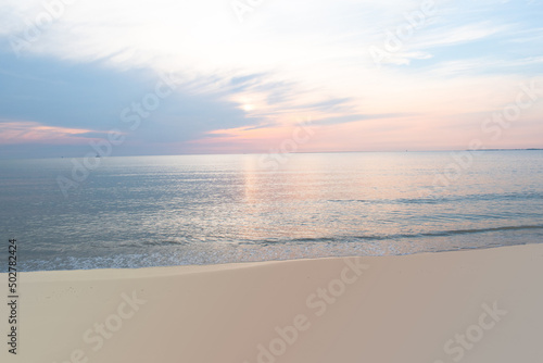 Colorful light pastel sky reflects onto ocean and sand in the early morning at the shore.