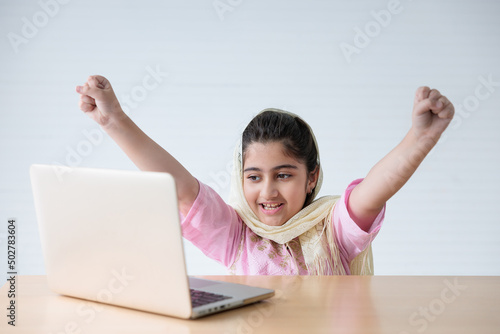 muslim girl using a laptop computer and raised hand for celebrating good news on the table © offsuperphoto