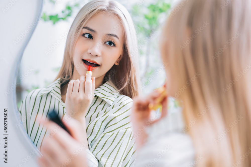 Young Asian woman applying lipstick in front of mirror Young Asian woman applying lipstick in front of mirror