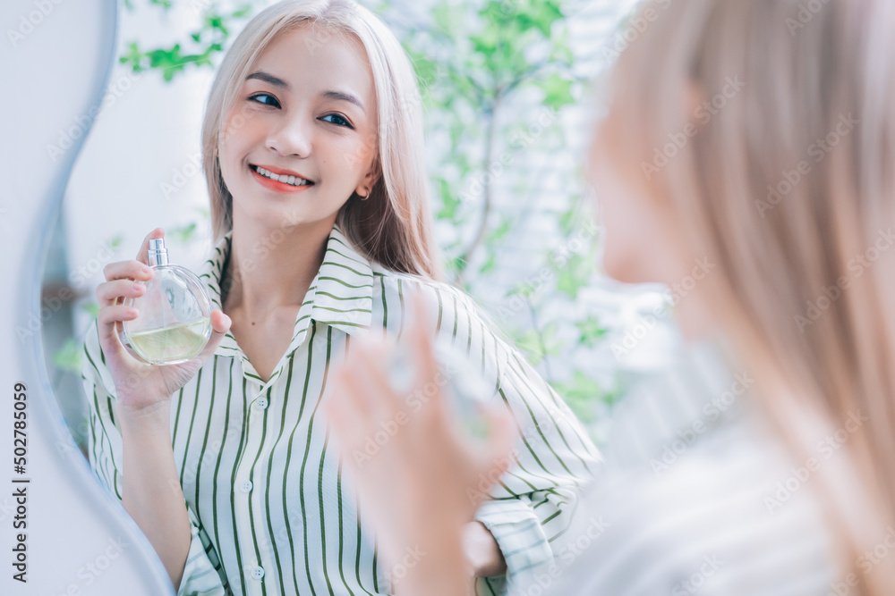 Young Asian woman spraying perfume in front of mirror