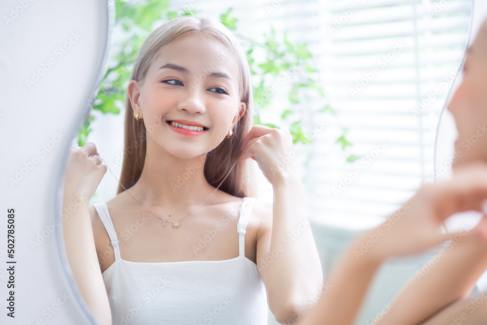 Young Asian woman wearing jewelry in front of mirror Young Asian woman wearing jewelry in front of mirror