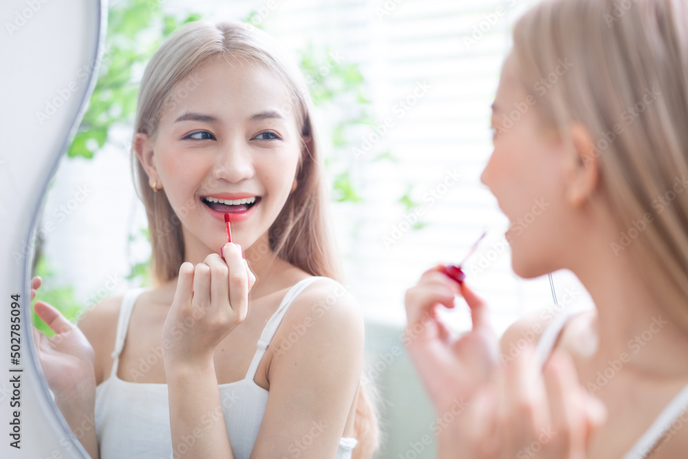 Young Asian woman applying lipstick in front of mirror Young Asian woman applying lipstick in front of mirror