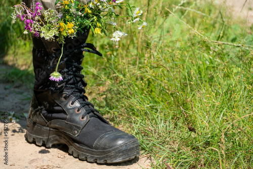 Black military boots with flowers. Concept - flowers instead of bullets and war. Ending the war in Ukraine. The surrender of the Russian army and the withdrawal of troops from the territory of Ukraine