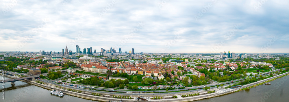 Historyczna panorama miasta z widokiem pod dużym kątem na kolorowe dachy budynków na rynku starego miasta. W tle widok na centrum nowoczesnej Warszawy z sylwetkami drapaczy chmur.