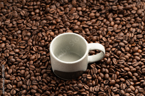Small empty coffee cup placed onto bed of roasted coffee beans close up