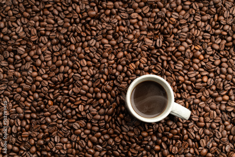 Small coffee cup filled up with hot coffee placed onto bed of roasted coffee beans flat lay view Small coffee cup filled up with hot coffee placed onto bed of roasted coffee beans flat lay view