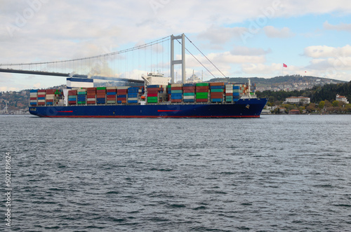 A cargo ship in the Bosphorus. Container ship with rows of containers. Concept of shipping containers by vessel. Cityscape with bridge over Bosphorus in the background