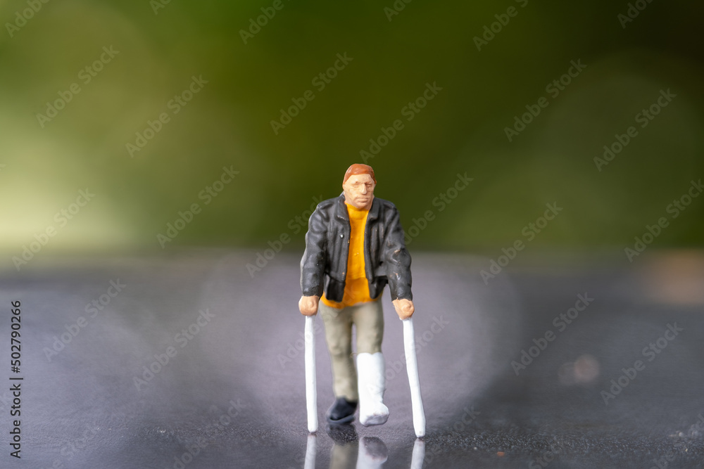 Miniature people man with broken leg is using crutch For Walking