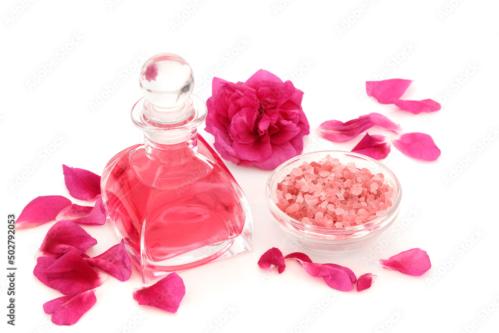 Rosewater in art deco glass bottle with flower, petals and Himalayan salt for exfoliation beauty treatment. Natural skincare concept to restore skin ph balance. On white background. Rosa rugosa. Rosewater in art deco glass bottle with flower, petals and Himalayan salt for exfoliation beauty treatment. Natural skincare concept to restore skin ph balance. On white background. Rosa rugosa.