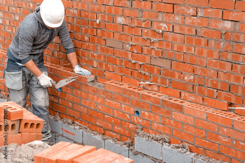Obraz na plátne Bricklayer laying bricks on mortar on new residential house construction