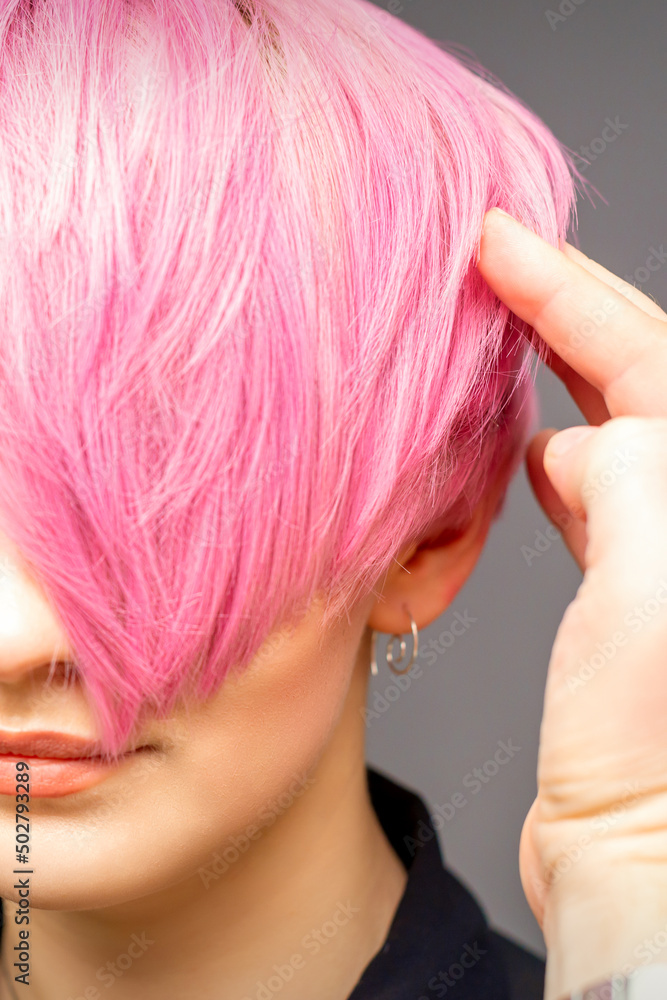 Fototapeta premium Hairdresser with hands and comb is checking out and fixing the short pink hairstyle of the young white woman in a hair salon
