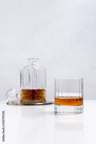 Un vaso de whisky con botella licorera sobre una mesa blanca y fondo claro 